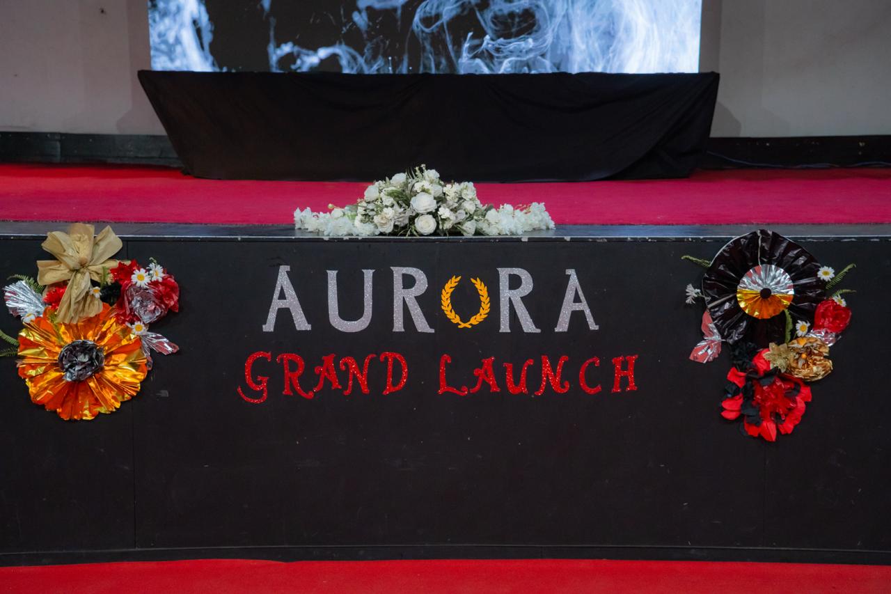 Aurora Grand Launch stage with floral arrangements, red carpet, and elegant event branding.