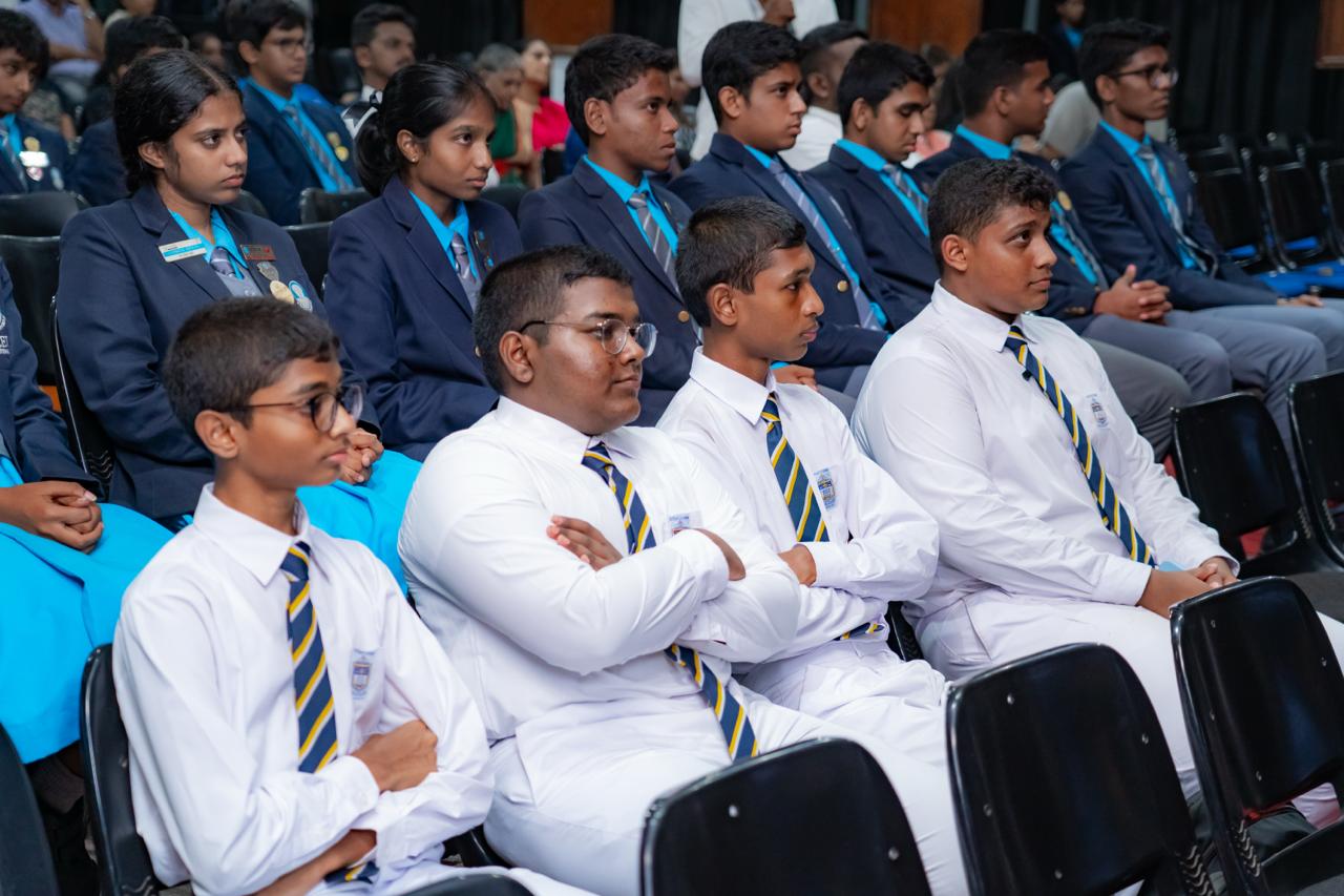 School assembly with students in uniforms, prefects in blazers, focused during an academic ceremony.