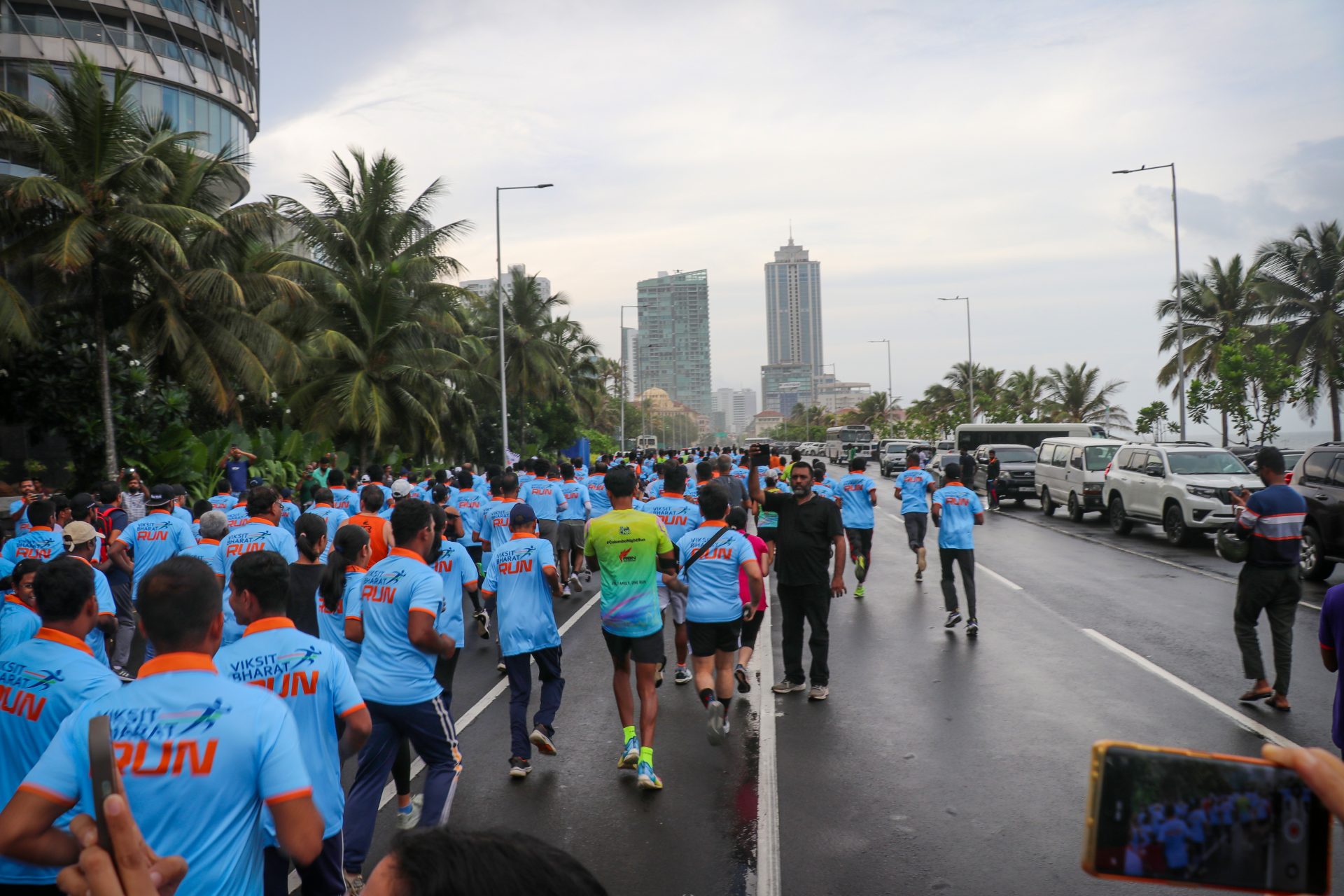 Mumbai city marathon participants running on palm-lined street, wearing Viksit Bharat Run blue shirts.