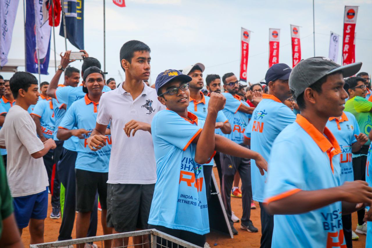 Group of runners warming up at outdoor charity fun run event, wearing blue shirts and smiling.