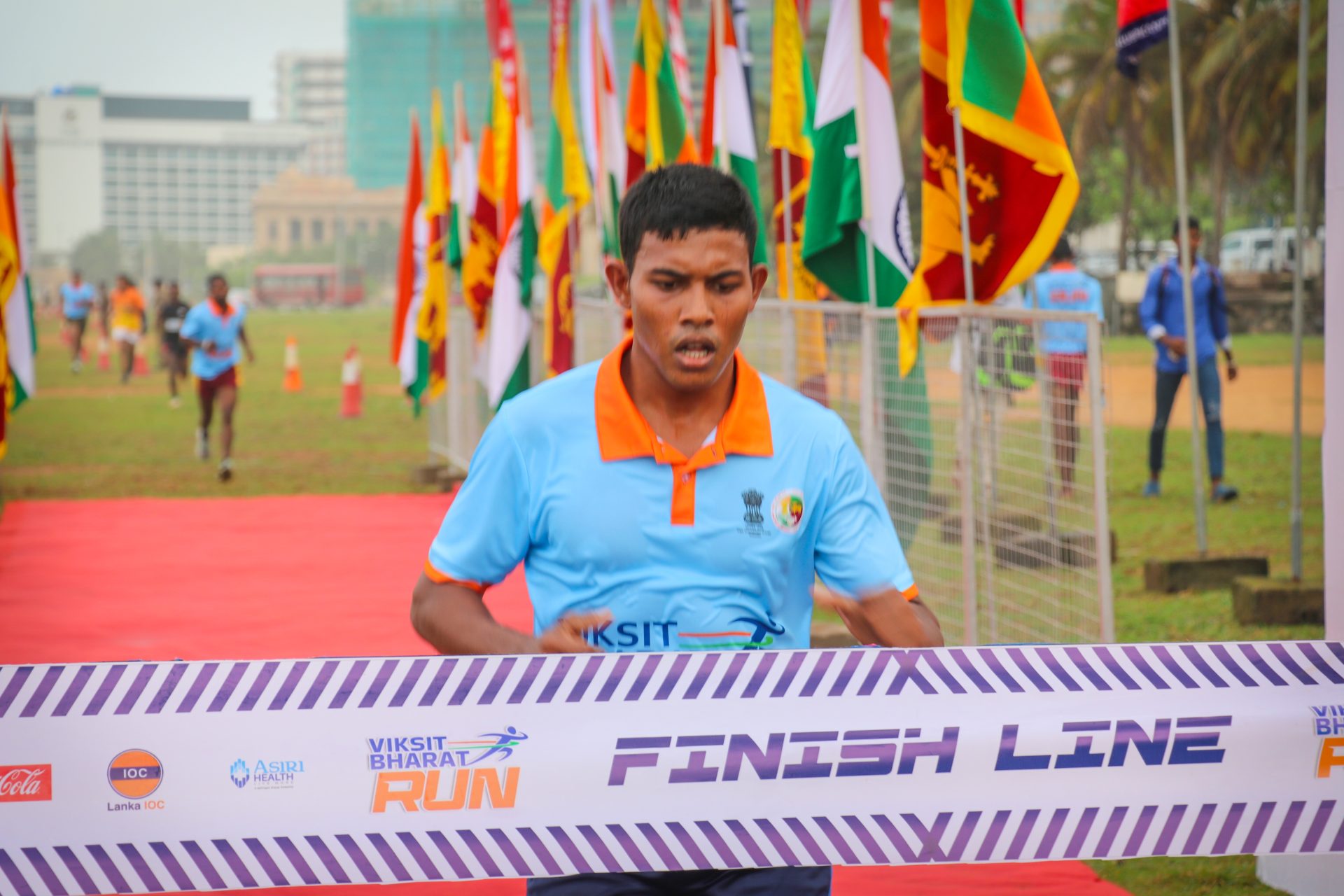 Runner wins Viksit Bharat Run international race, crossing finish line with flags and sponsors visible.