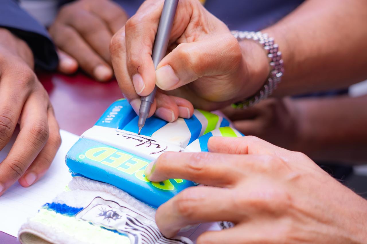 Cricket fan gets glove autographed by player at sports event, close-up signing moment.