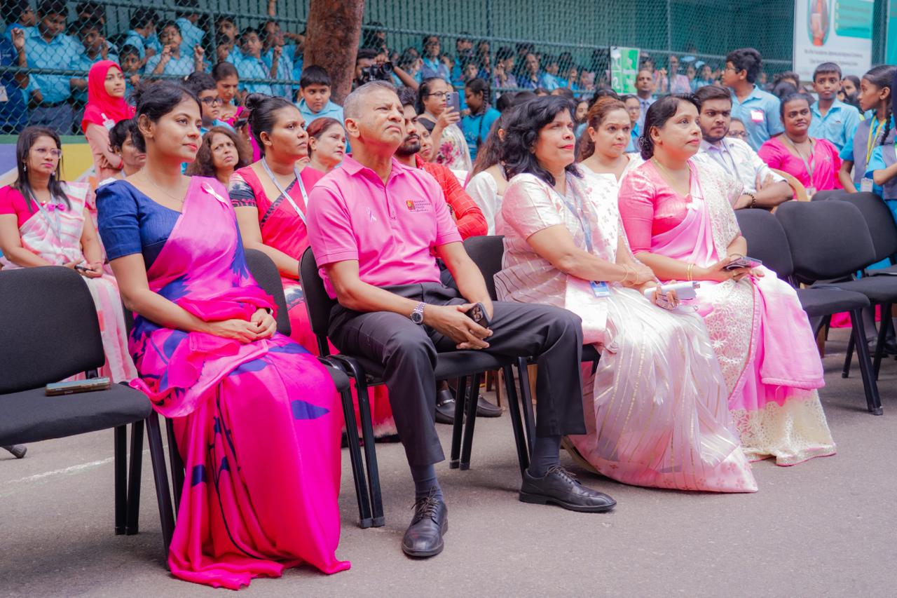 Breast cancer awareness event with adults in pink attire and students in blue uniforms outdoors.