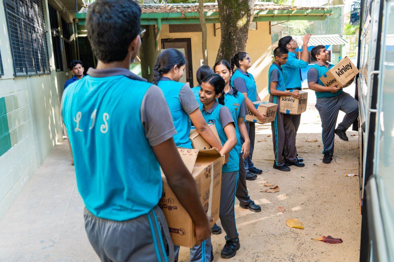 Students in uniforms form a human chain to load Kinley water boxes onto a school bus.