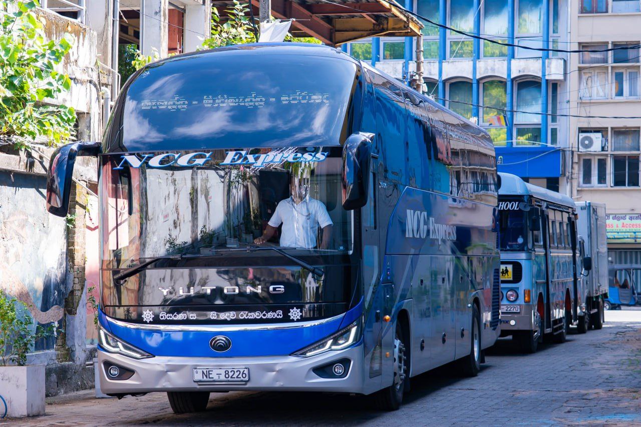 Modern Sri Lanka city street with NCG Express Yutong bus and school bus parked roadside.