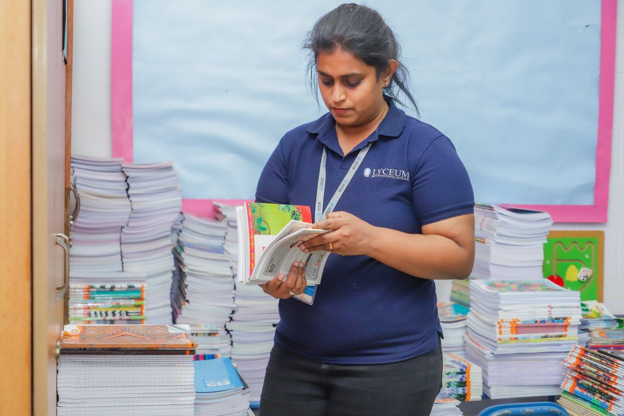 Lyceum International School teacher organizing colorful textbooks in classroom for student distribution.