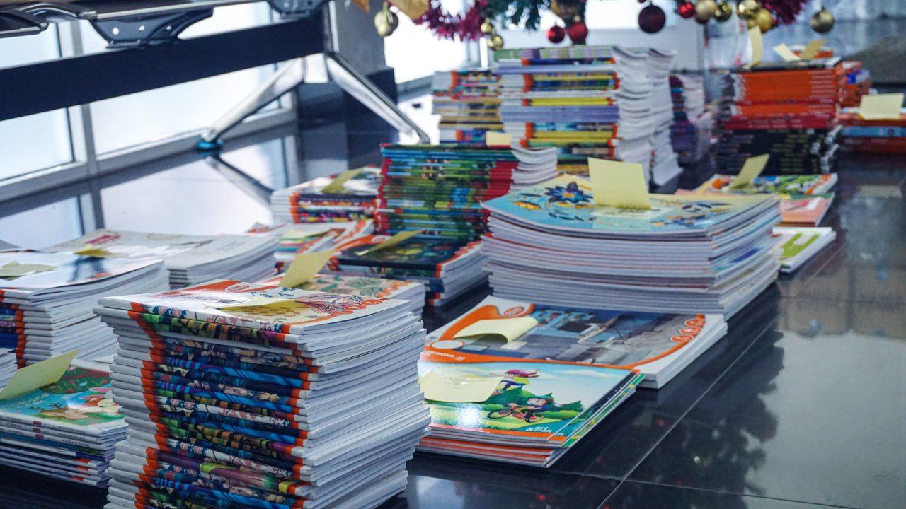 Stacks of childrens books organized with sticky notes for festive holiday distribution in a bright lobby.
