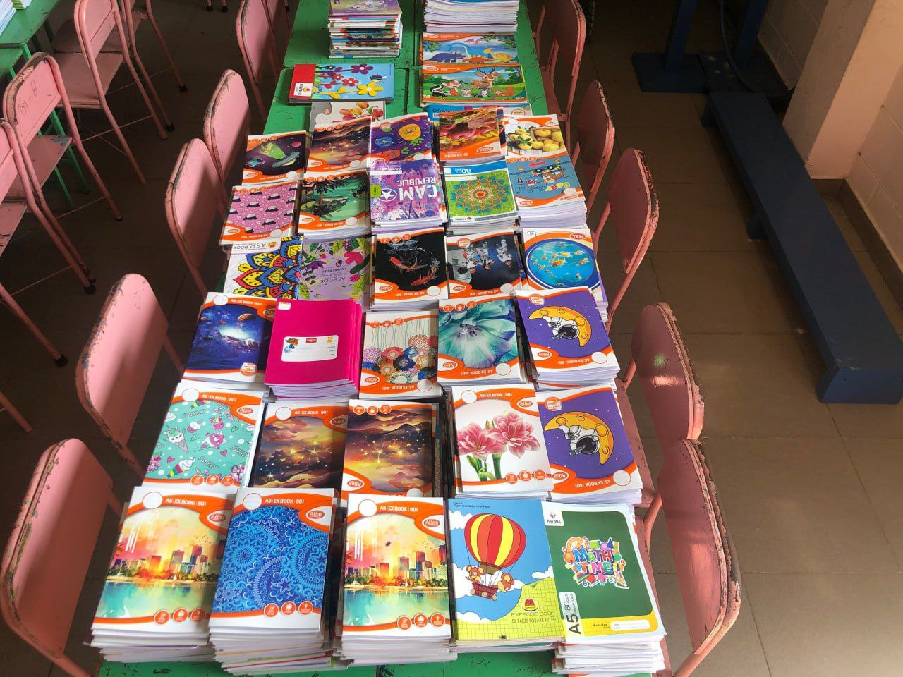 Colorful student notebooks stacked on a classroom table ready for back-to-school distribution.