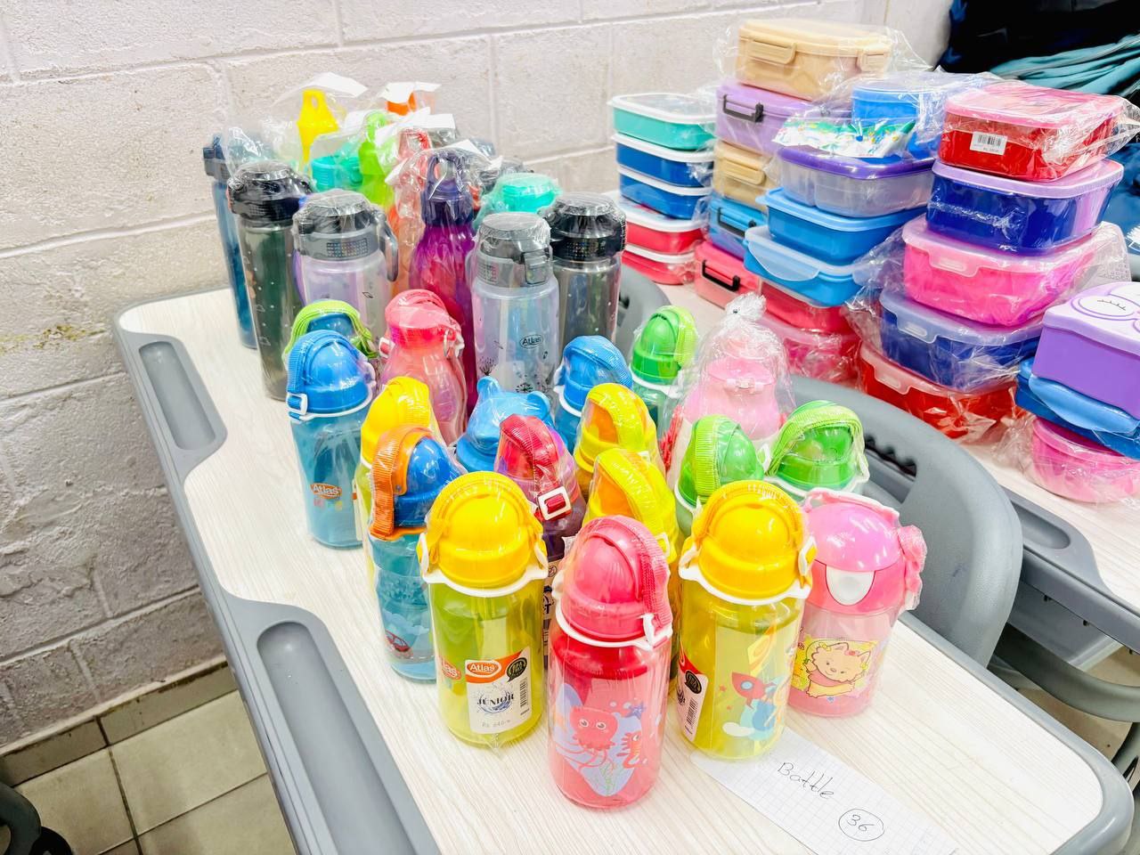Colorful kids water bottles and lunch boxes on a table for school supplies sale or distribution.