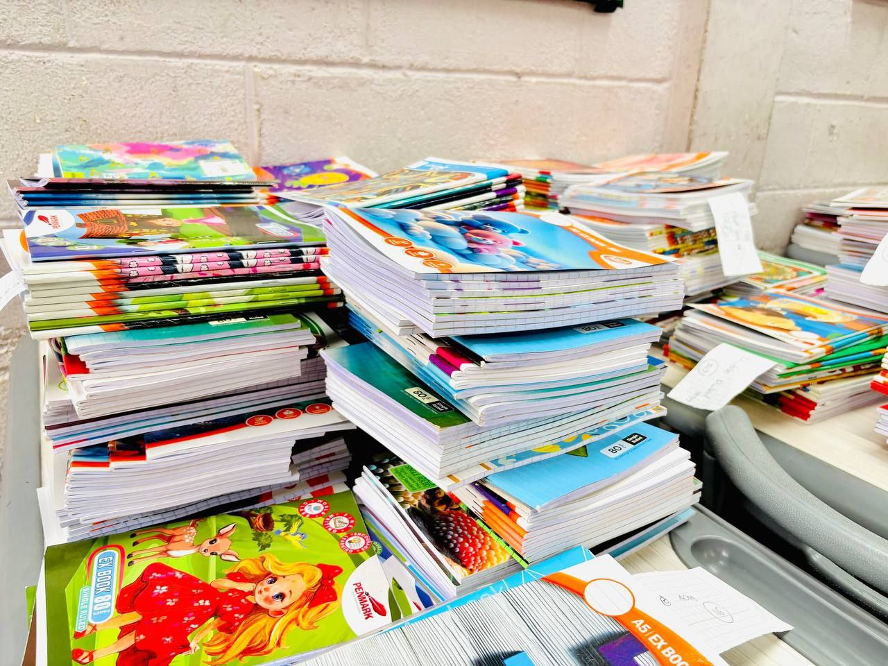 Colorful childrens exercise books and notebooks stacked on a classroom desk, ready for school distribution.
