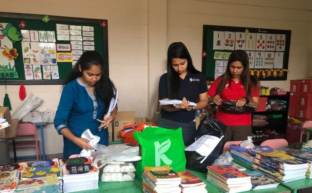 Teachers packing school supplies in classroom with educational posters, creating student resource kits.