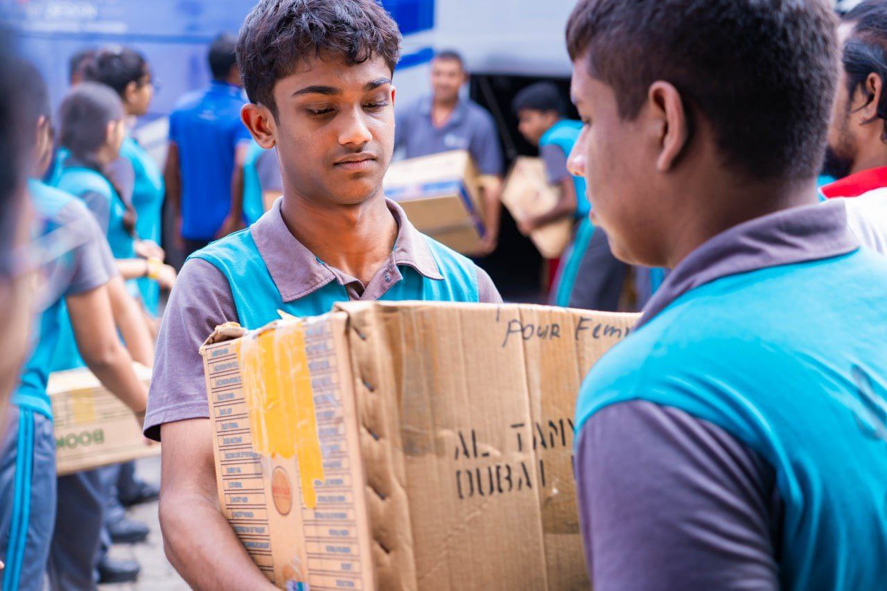 Young volunteers in blue vests teamwork to load donation boxes in Dubai community service event.