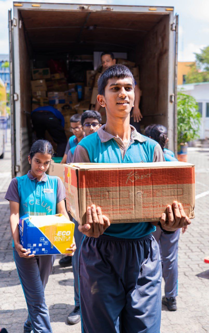 Students in school uniforms unloading boxes from a truck during a community service project.
