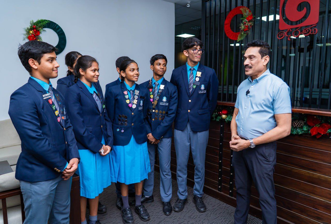 Lyceum students in school uniforms receive awards from teacher during holiday event in decorated office.