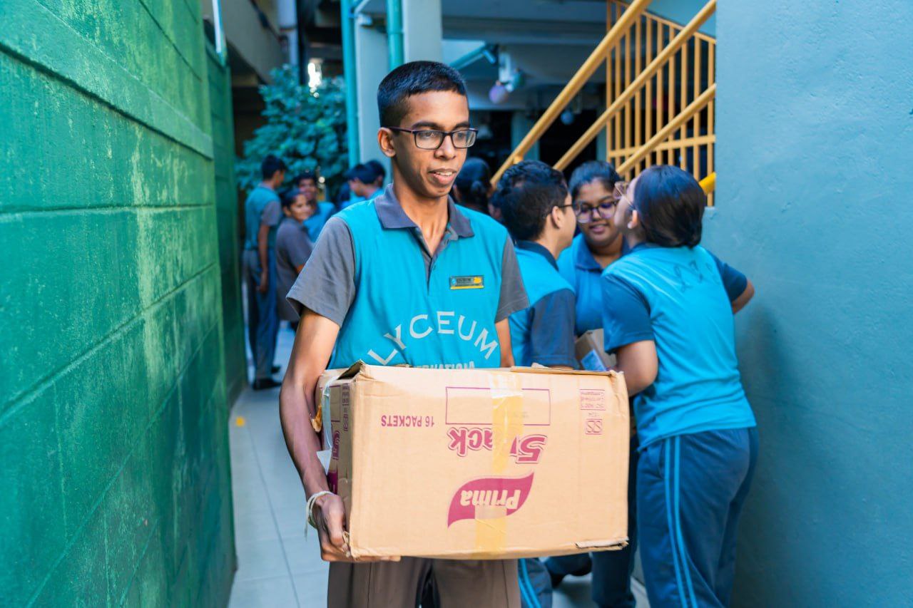 High school students in blue uniforms carrying boxes during a teamwork community service project.