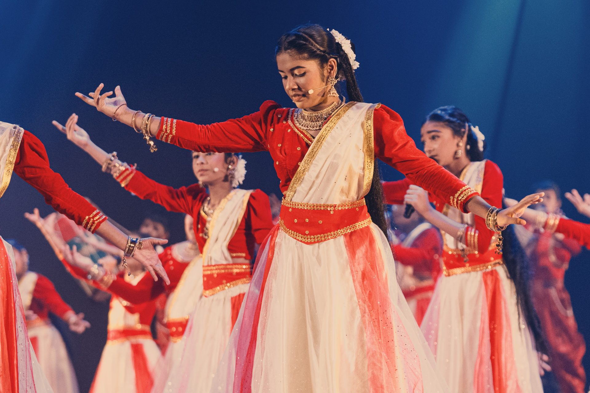 Indian classical dance performance with children in traditional costumes, jewelry, and vibrant stage lighting.