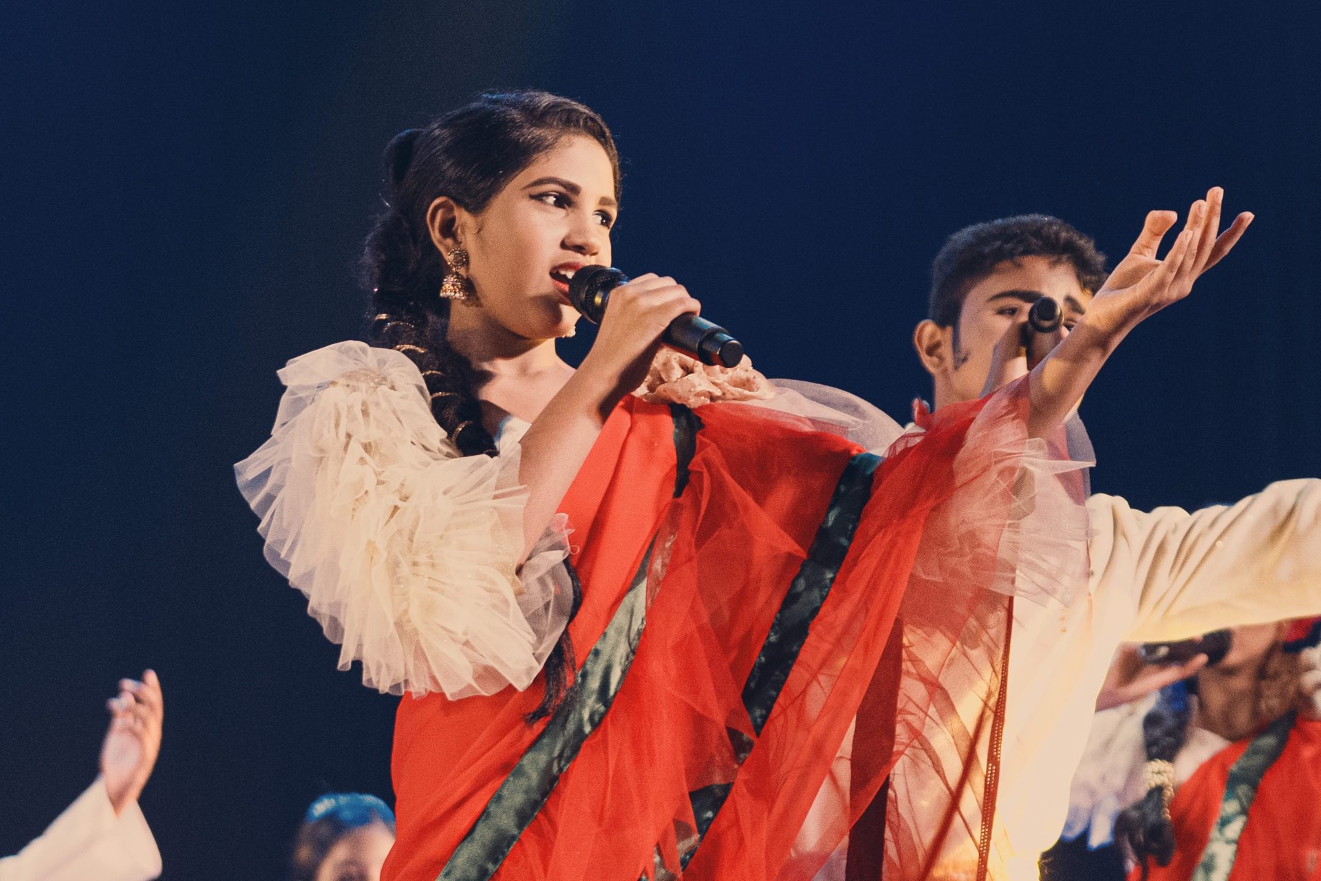 Indian singers performing on stage in colorful sarees and traditional attire during a cultural event.