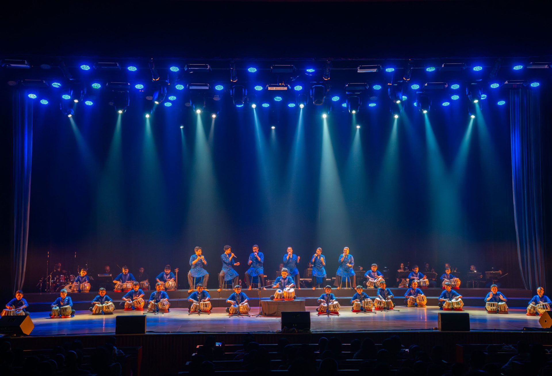 Indian tabla ensemble performing on stage with blue lighting at a cultural music festival event.