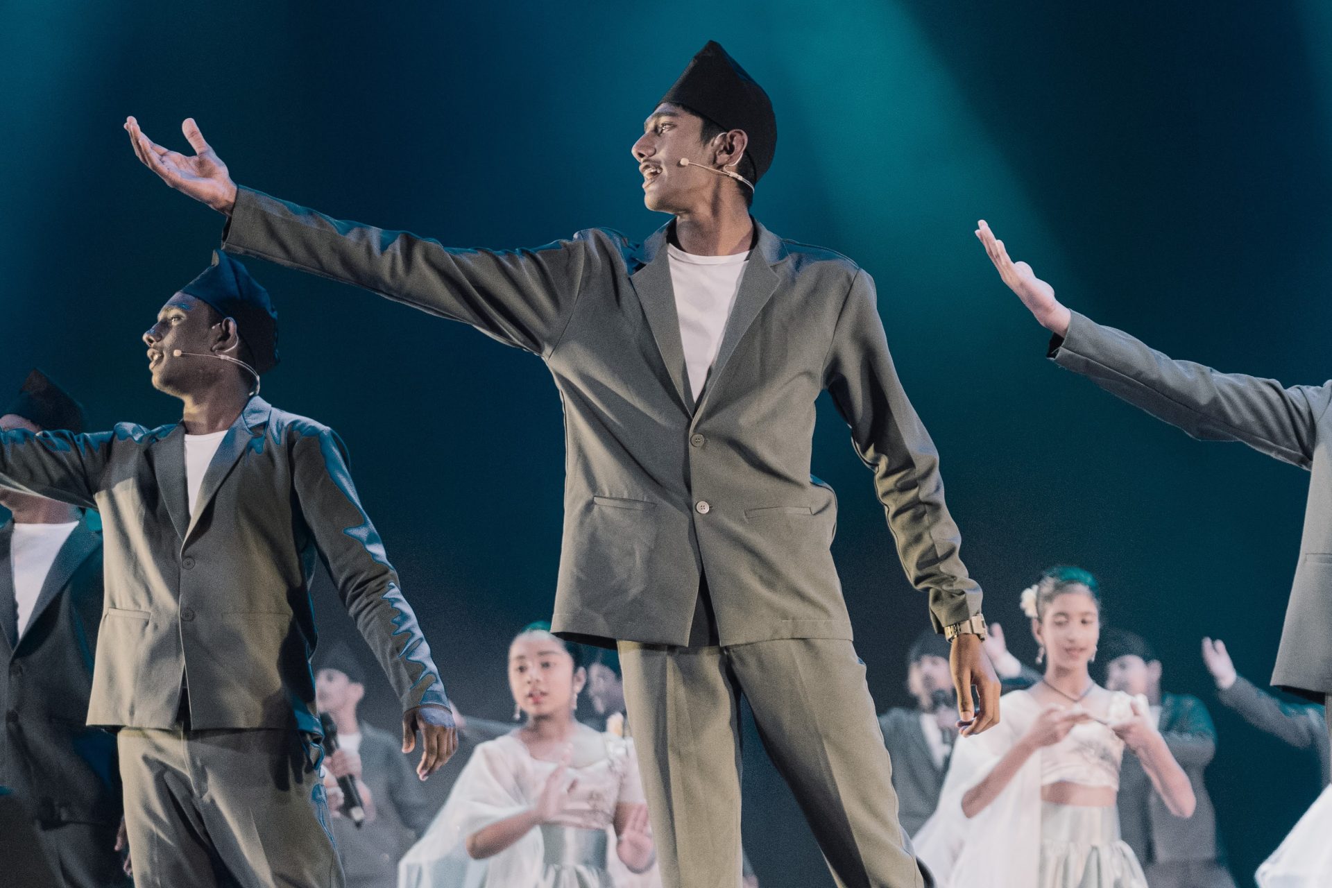 Cultural stage performance with male and female dancers in traditional costumes and dramatic blue lighting.