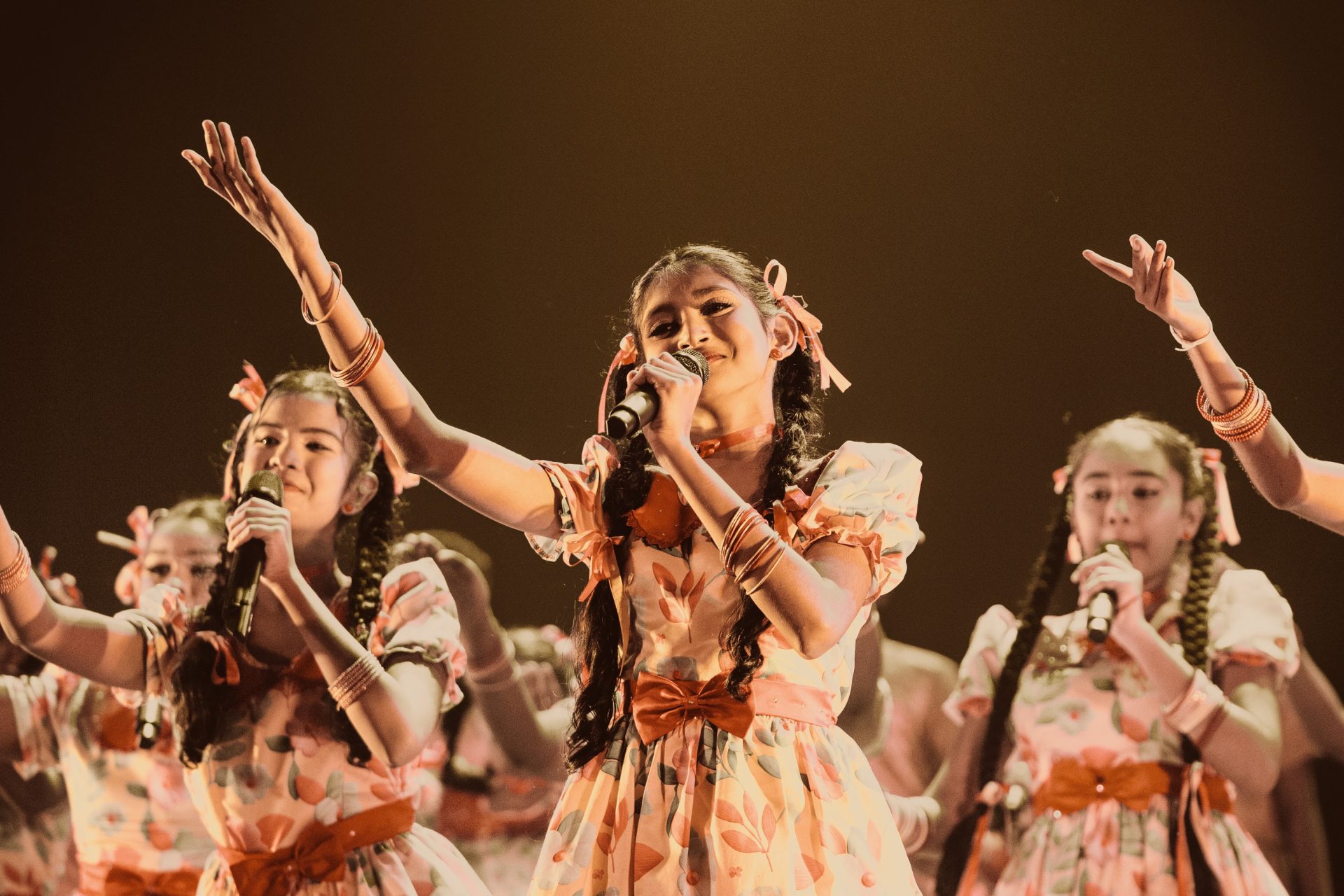 Young girls in matching costumes sing and dance on stage during a lively musical performance.