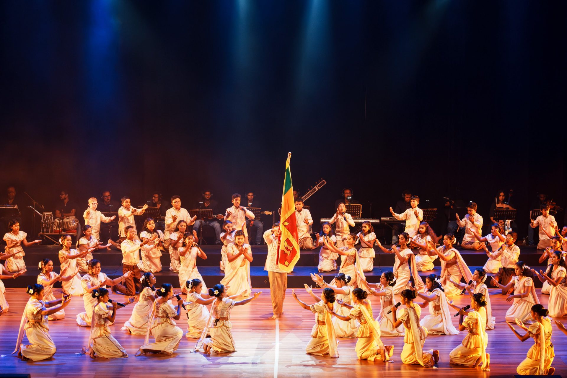 Sri Lankan children performing traditional dance with national flag on stage during cultural celebration.