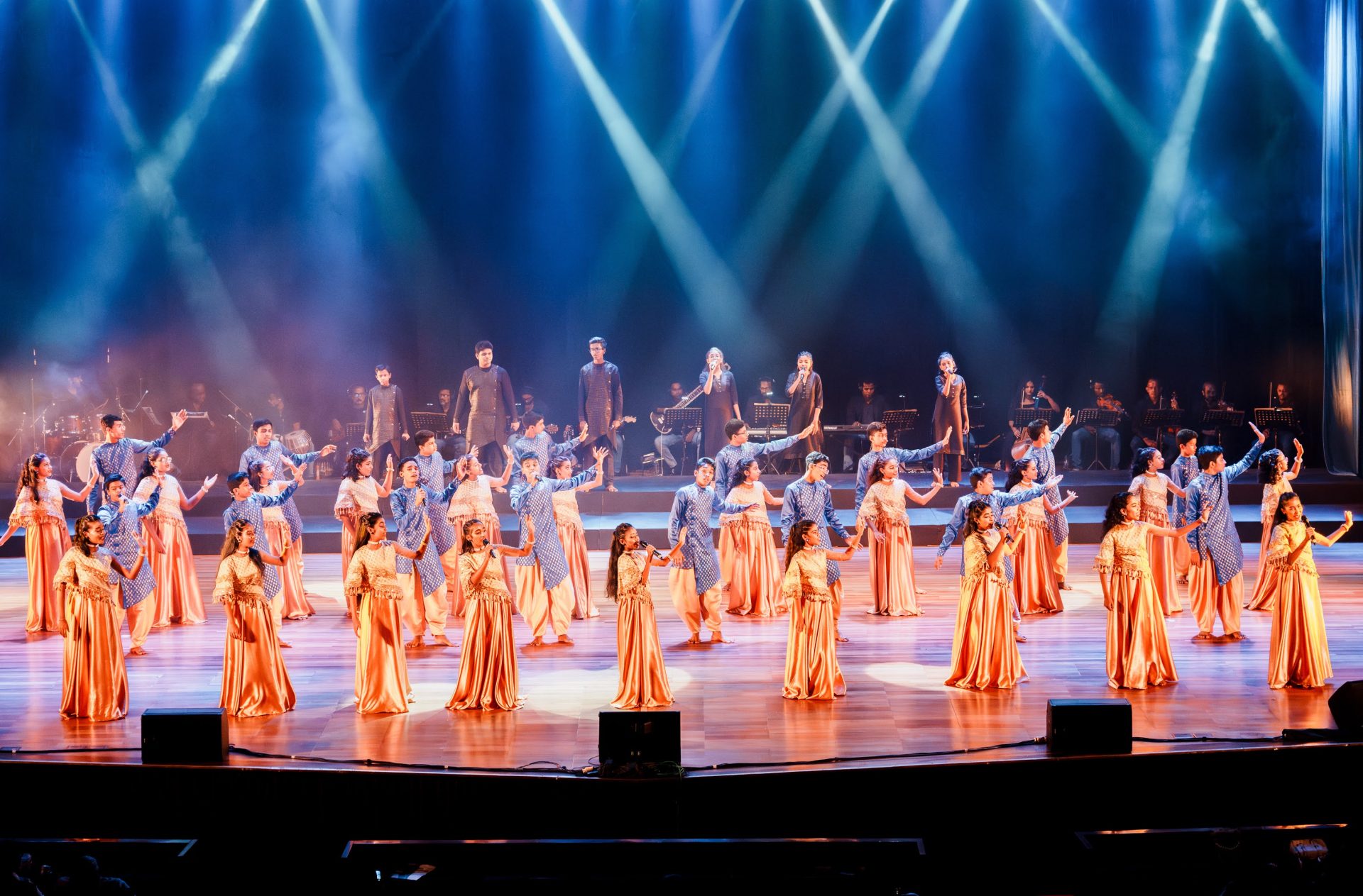 Grand Indian dance performance with musicians, singers, blue stage lights, and colorful costumes in celebration.