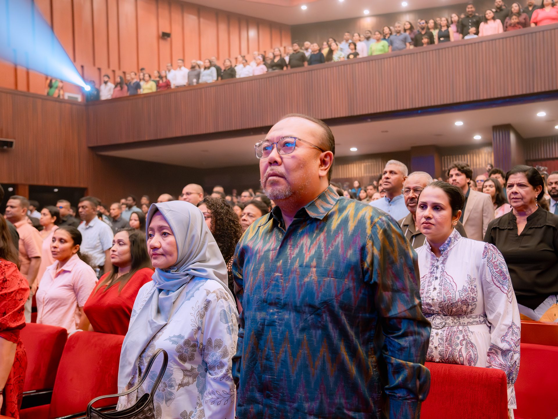 Diverse audience in formal attire attending a significant event in a modern, well-lit auditorium.