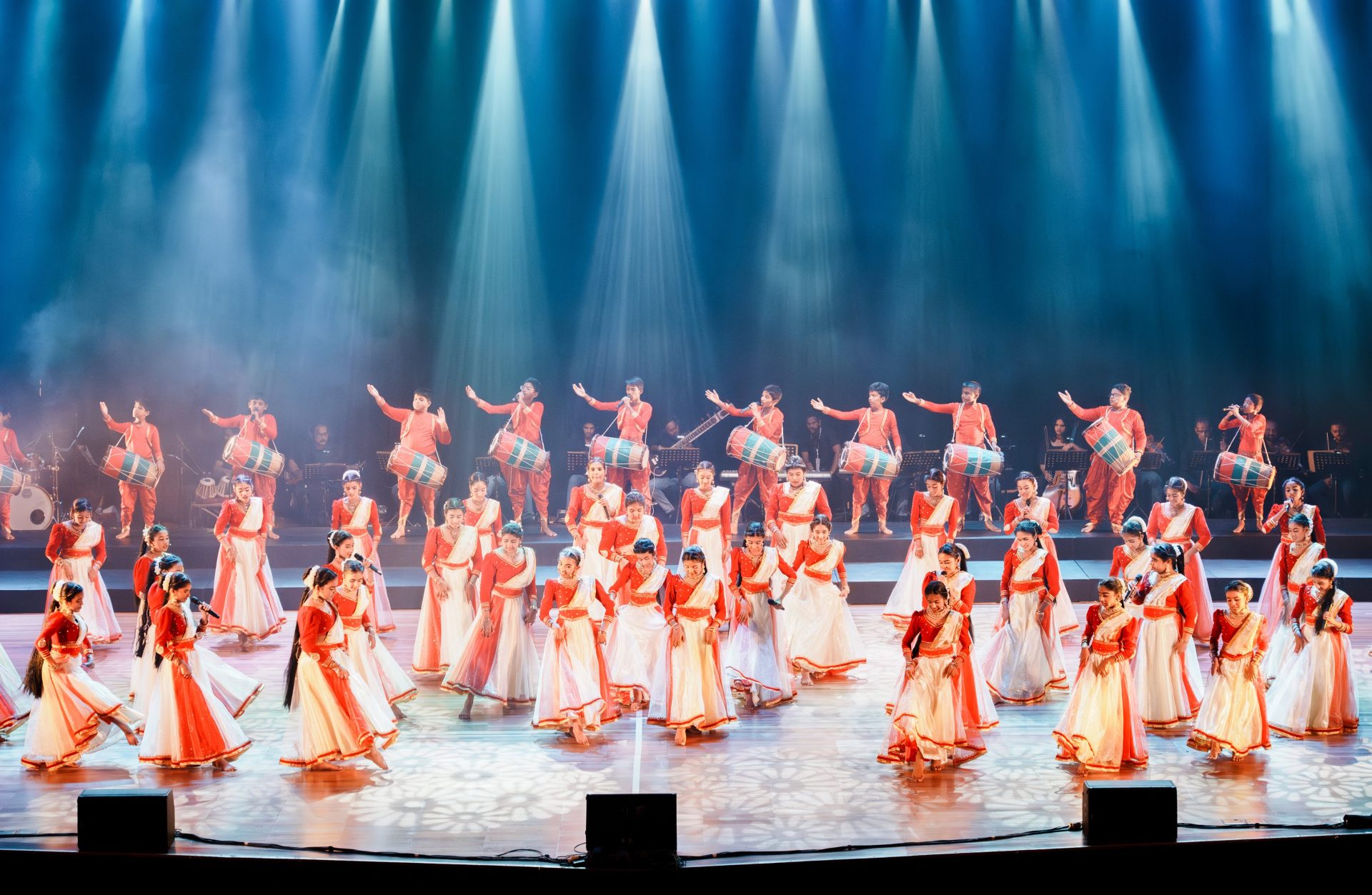 Traditional Indian dancers and drummers perform on stage in colorful costumes under dramatic lighting.