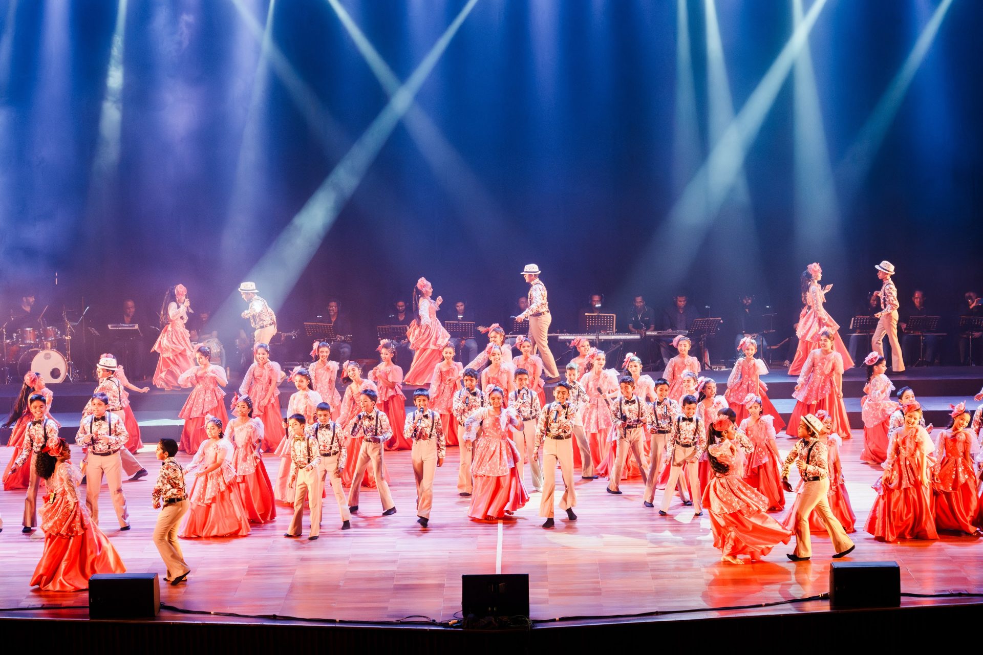 Colorful traditional dance performance on stage with vibrant costumes, live musicians, dramatic lighting, and choreography.