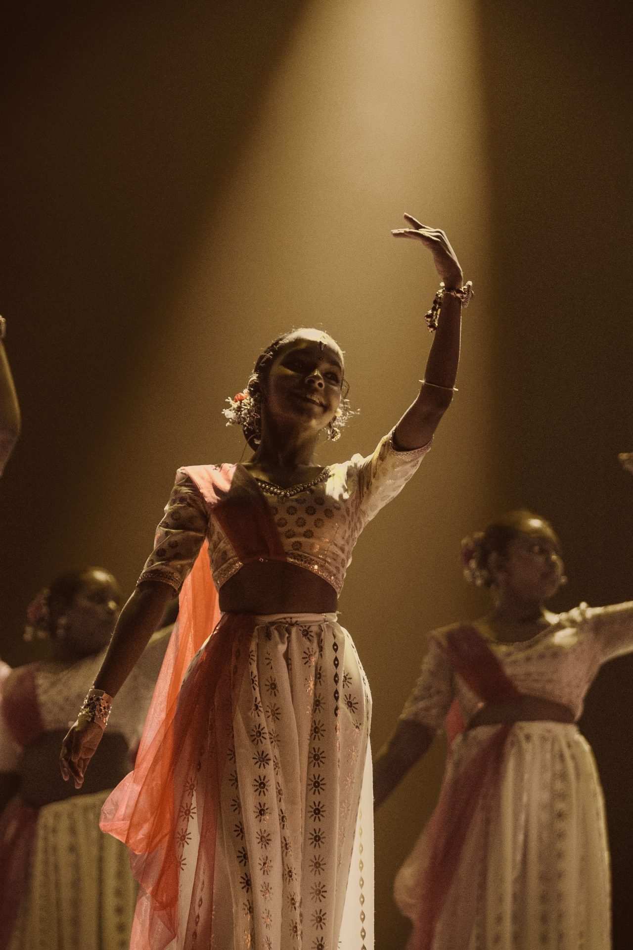 Indian classical dancers performing on stage in traditional attire under dramatic golden lighting.