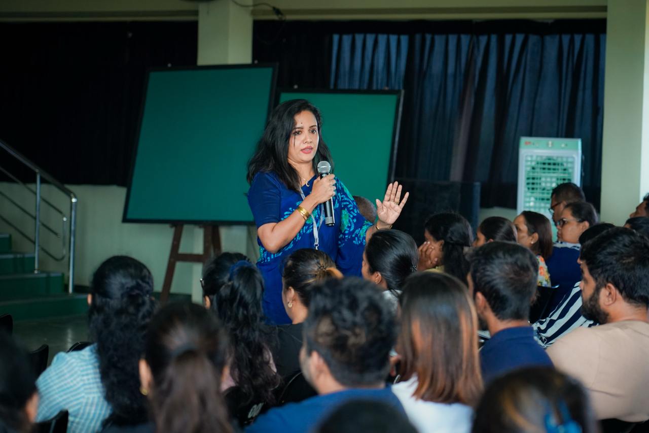 Woman in blue leading interactive seminar, engaging young adult audience in classroom with chalkboards.