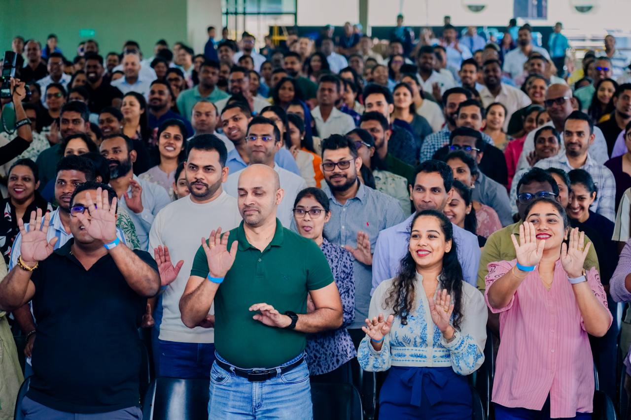 Diverse group at indoor workshop, smiling and raising hands together in team-building activity.
