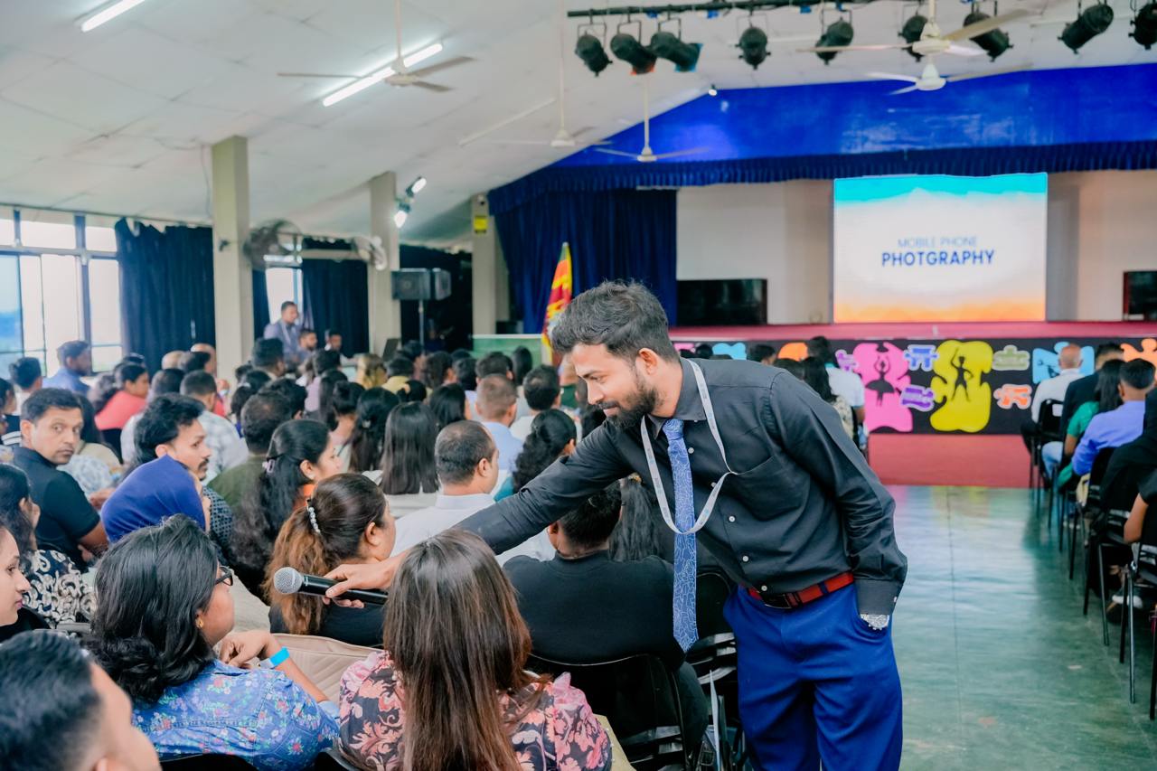 Presenter engaging audience at mobile photography workshop in bright, spacious hall with stage and screen.