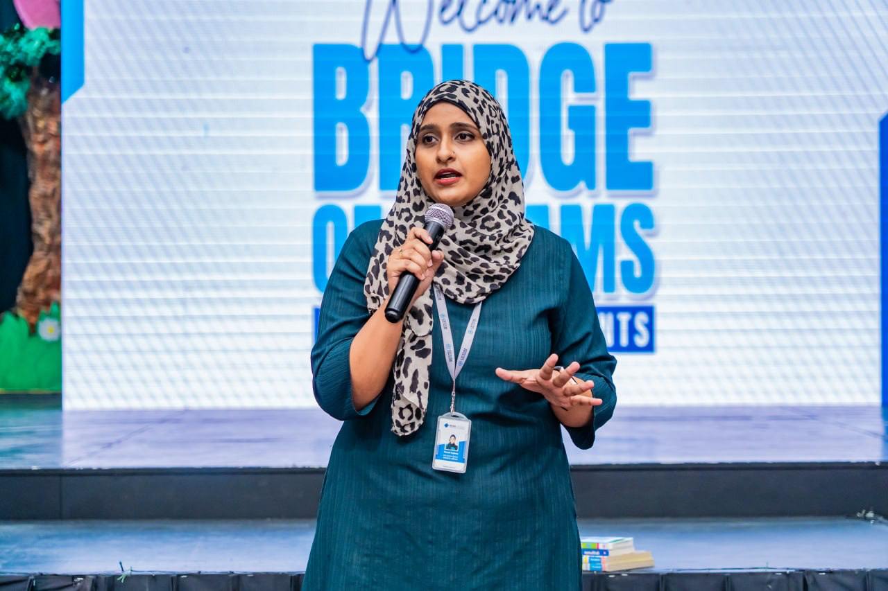 Muslim woman in hijab speaks at Bridge of Dreams conference, inspiring audience on stage.