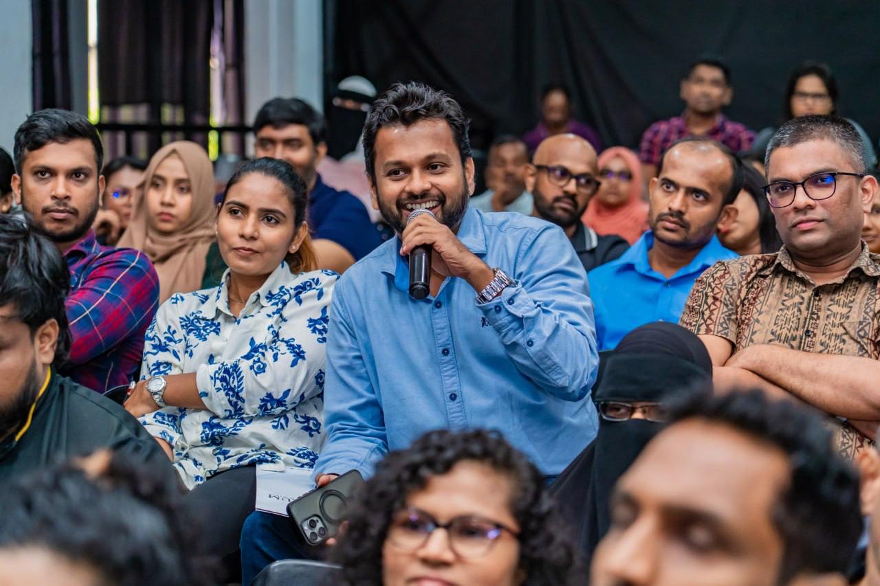 Smiling man with microphone engages diverse audience at interactive seminar discussion.