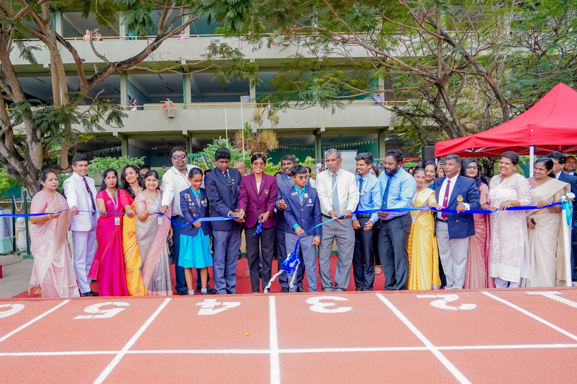 Ribbon-cutting ceremony with students, teachers, and dignitaries on a newly opened school running track.