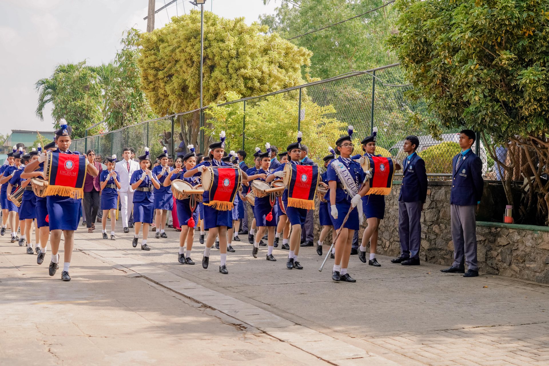 Lyceum school marching band parade with student leaders, drums, uniforms, and banners outdoors.