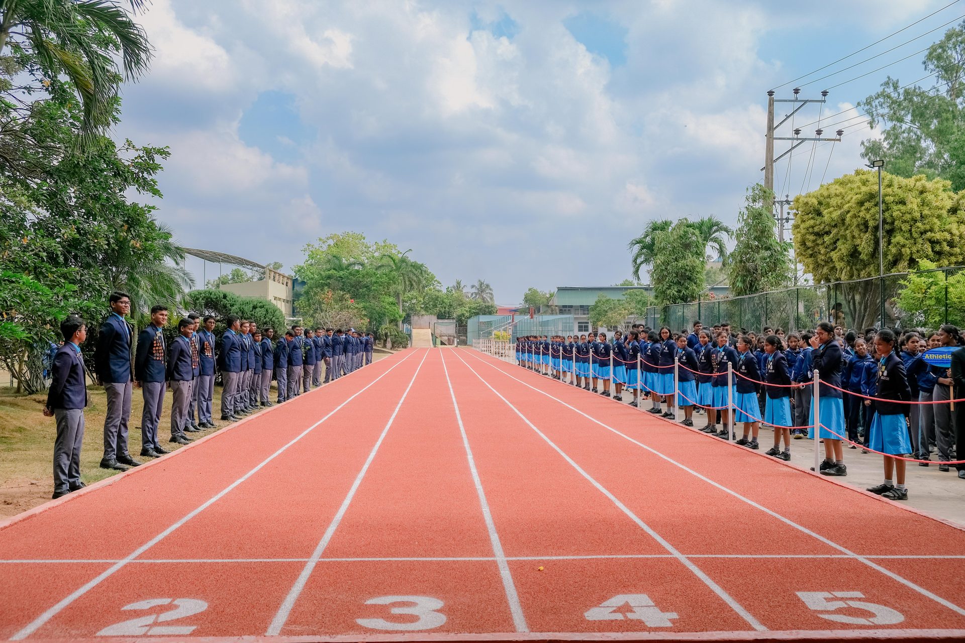 Uniformed students line a bright orange track, ready for a school sports day ceremony outdoors.