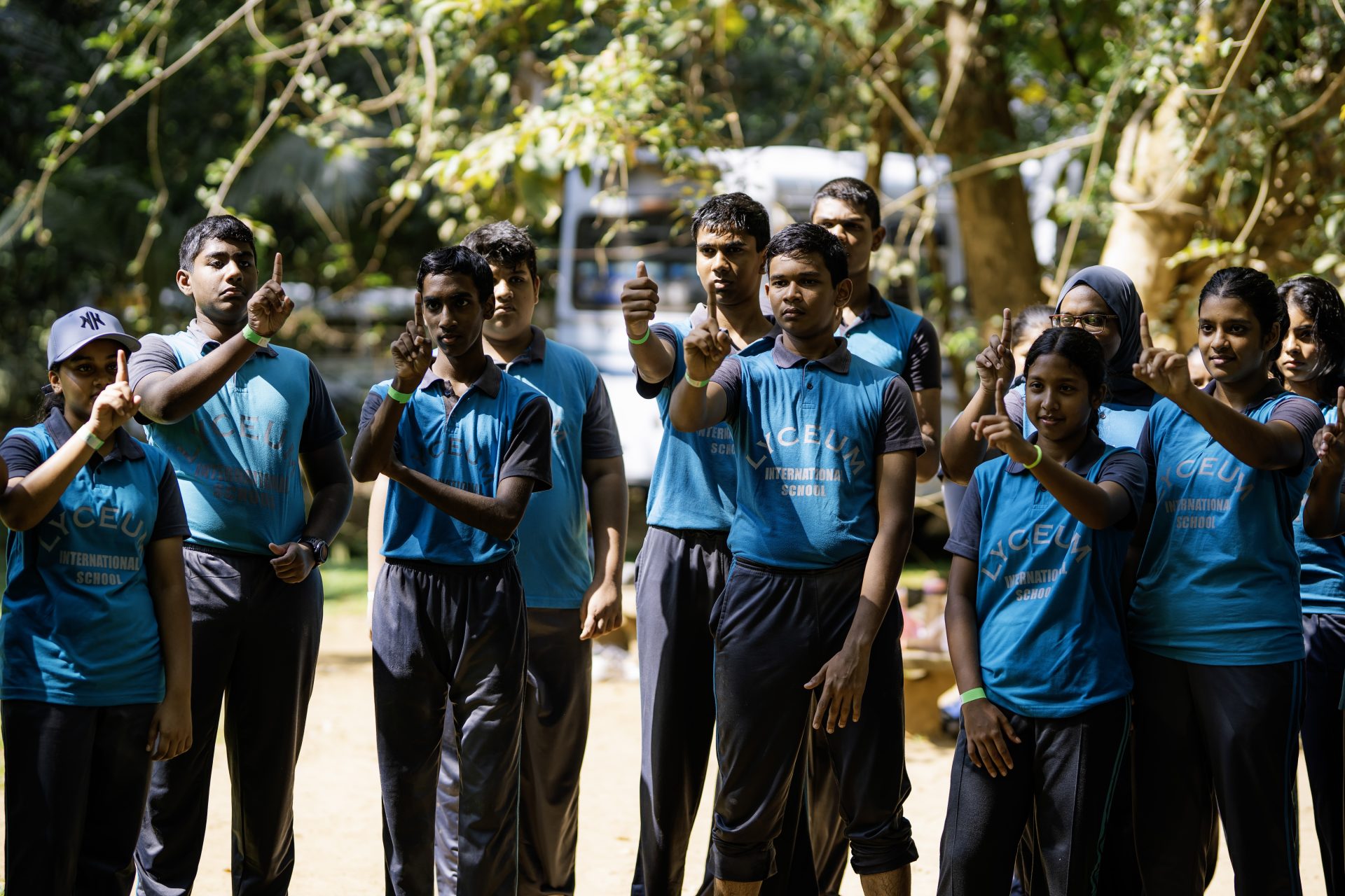 Lyceum students in blue uniforms make unity gesture during outdoor team-building activity in park.