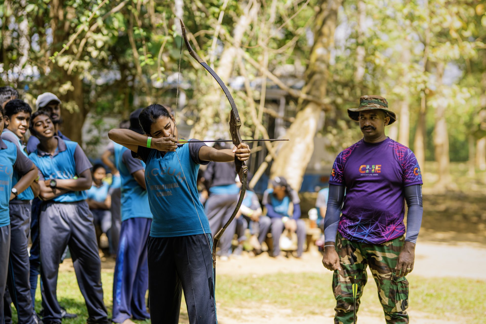 Girl aiming bow in outdoor archery lesson with instructor and classmates at school camp.
