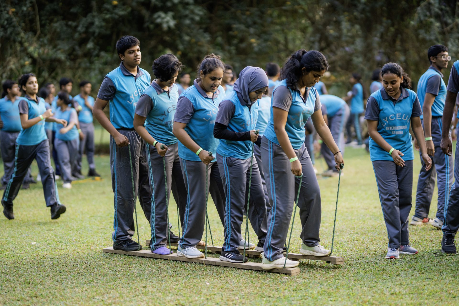 Lyceum International School students coordinate on wooden planks in an outdoor teamwork challenge.