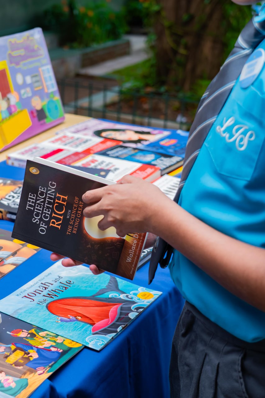 Man in blue shirt selects The Science of Getting Rich at outdoor book fair with diverse books.