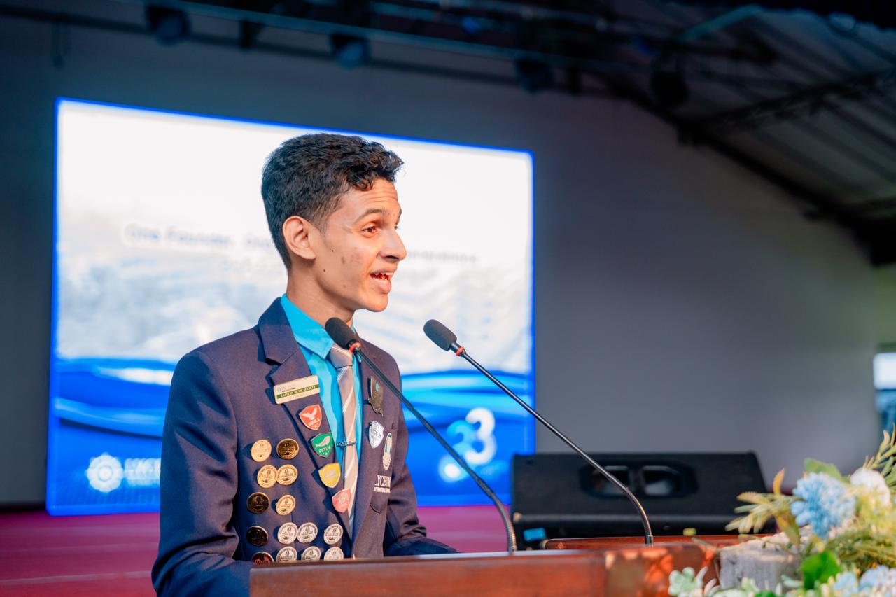 Young leader in navy blazer gives speech at podium during international youth conference.