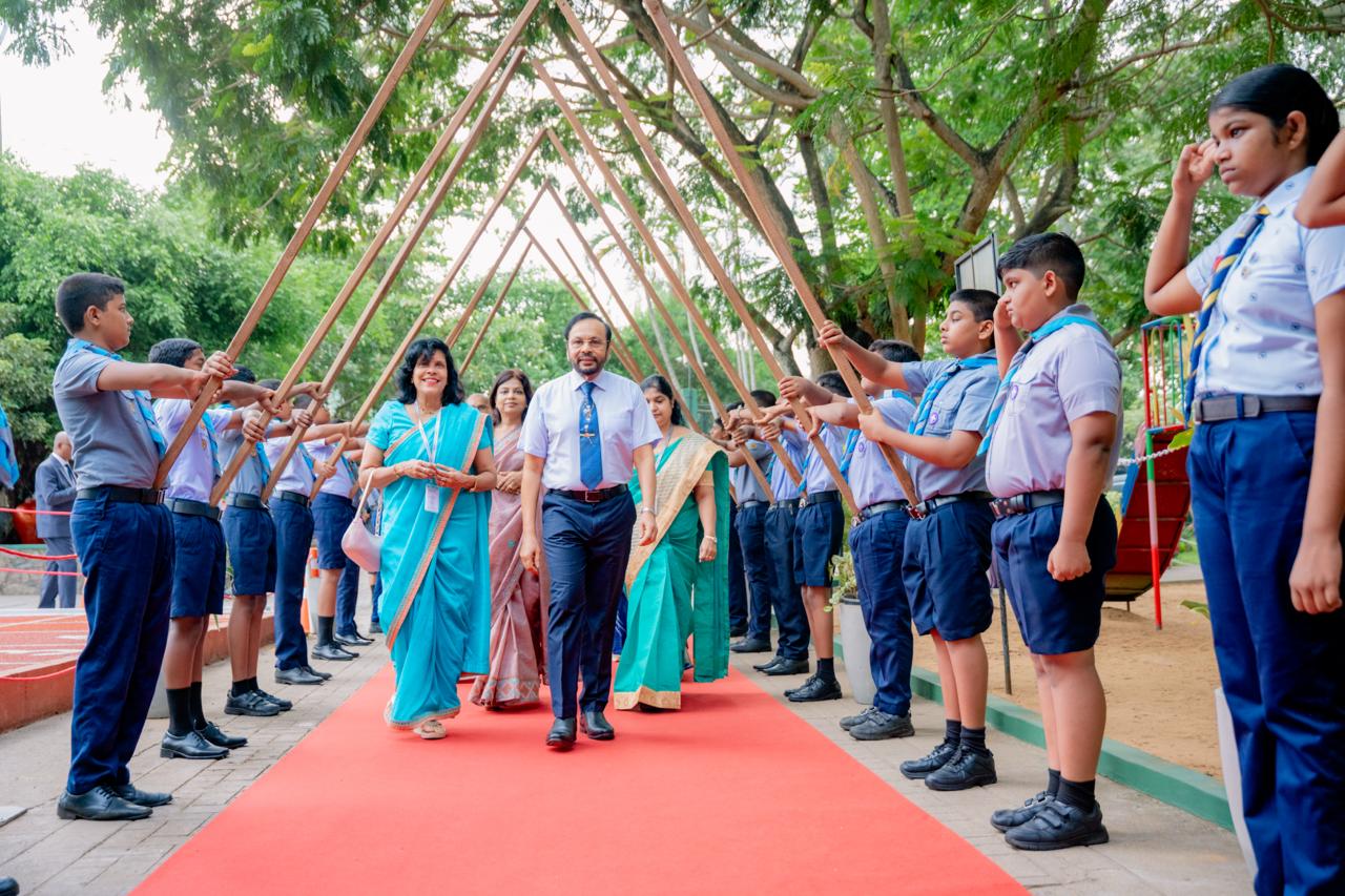 School officials walk a red carpet as students in uniforms form a ceremonial arch outdoors.
