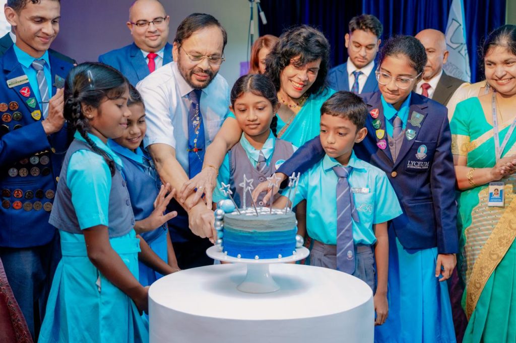 Students and teachers joyfully cut a blue cake together at a school celebration ceremony.