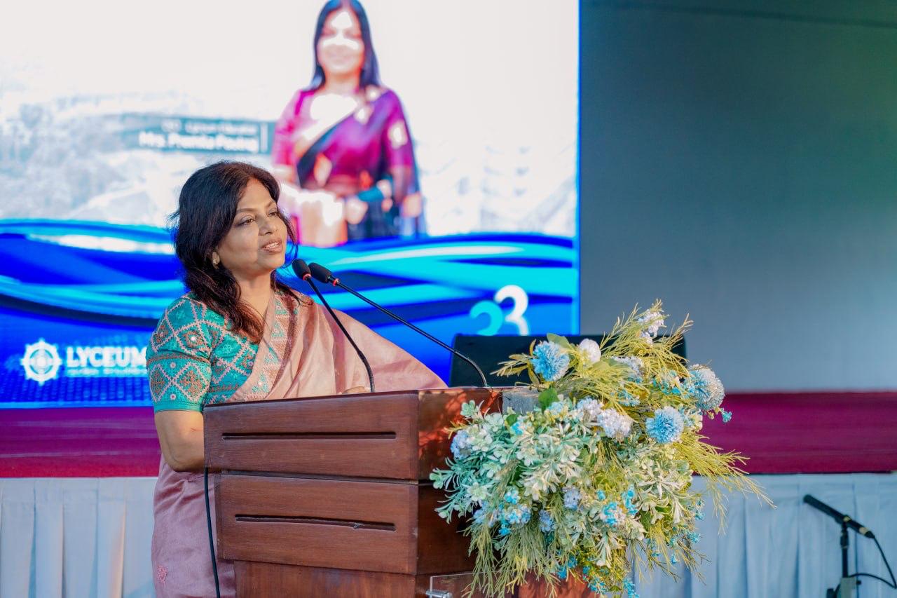 Woman in saree delivers keynote speech at Lyceum 2023 podium with floral arrangement.