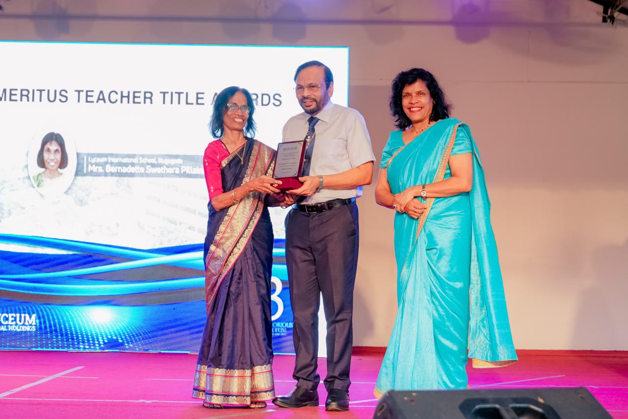 Mrs. Bernadette Swethra Pillai receives Emeritus Teacher Award on stage with colleagues during ceremony.