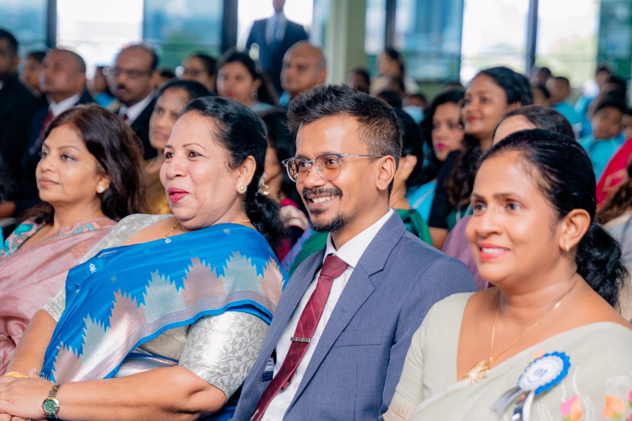 Professionals in sarees and suits smile at a formal Indian awards ceremony in a bright hall.