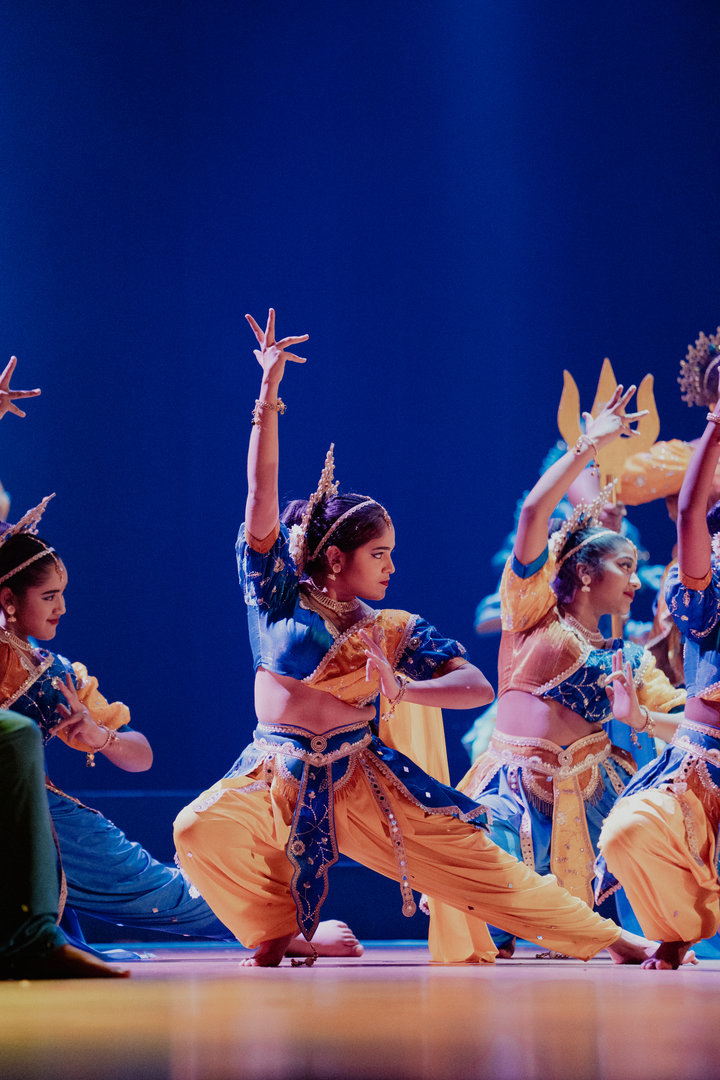 Energetic Indian Classical Dance Troupe in Vibrant Costumes Women perform Indian classical dance on stage in colorful yellow and blue costumes with dramatic lighting.