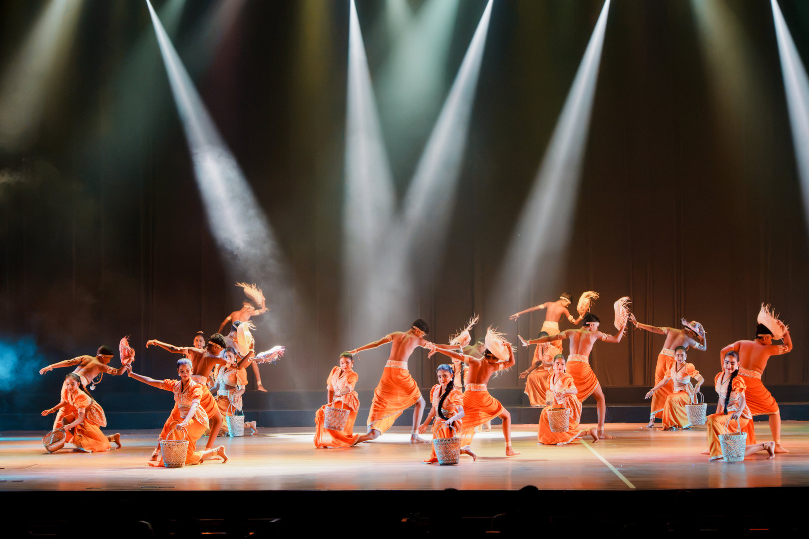Vibrant Orange Dance Ensemble Under Dramatic Stage Lights Dancers in orange costumes perform energetic cultural dance under dramatic stage lighting with traditional props.